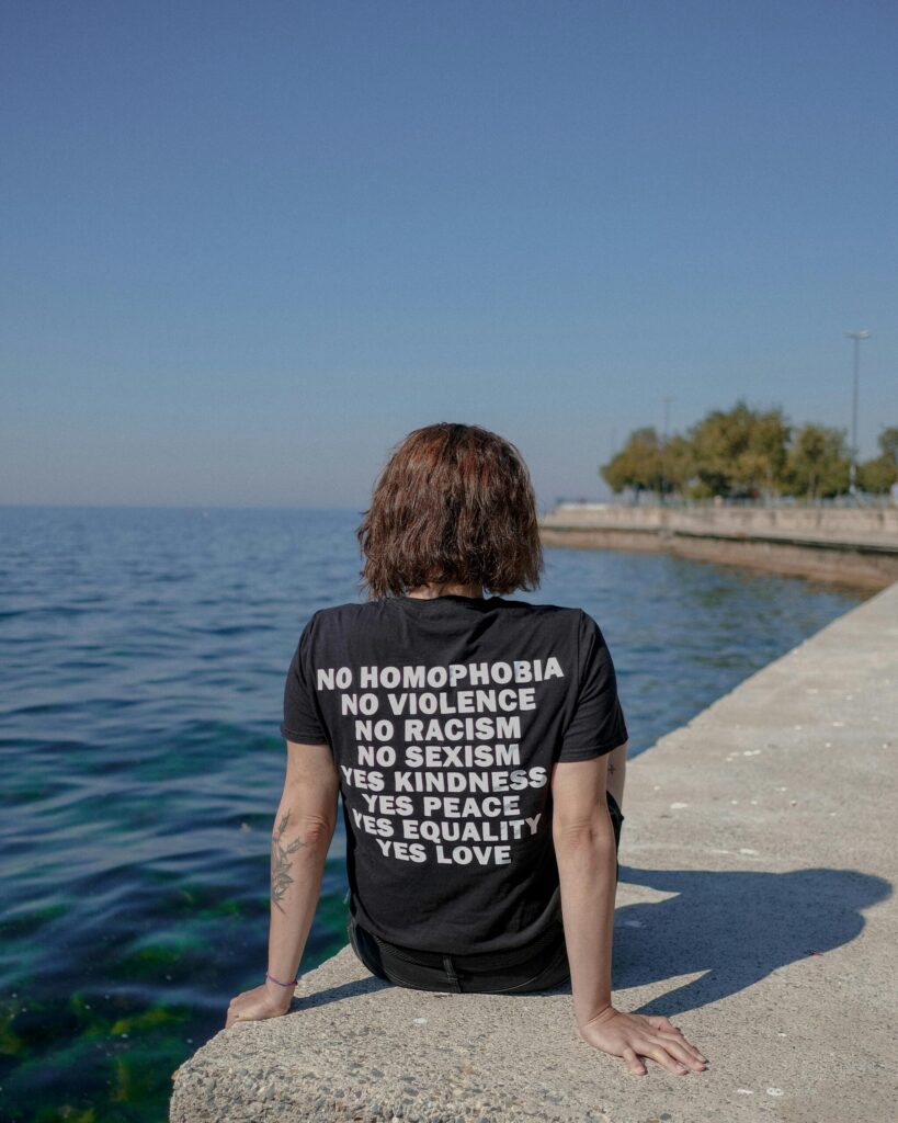 Back view of a person sitting by the sea in Istanbul, wearing a shirt with equality slogans. Bright day.